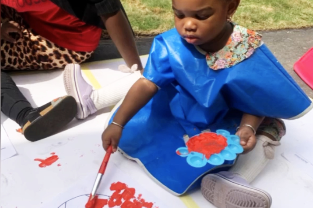 Little 3 year old girl is sitting on the floor painting a ball